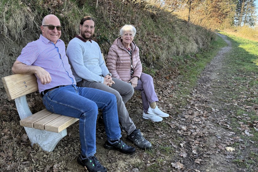 Der Verein "Arbeits-Gemeinschaft Menschen mit Handicap" hat dank Spenden mittlerweile zehn Ruhe-Bankerl im Gemeinde-Gebiet von Scheyern aufgestellt. Das zehnte Exemplar findet sich am Pudelbach-Wegerl zwischen Mitterscheyern und Hammerschmied-Weiher. Zum "Probe-Sitzen" kamen hier nach dem Aufstellen zusammen: Spender Wolfgang Inderwies (links), Geschäftsführer Miguel Pérez Taboaga von der "Gerlsbeck Zimmerei Holzbau GmbH & Co. KG" sowie Bank-Patin Tilly Grubwinkler.